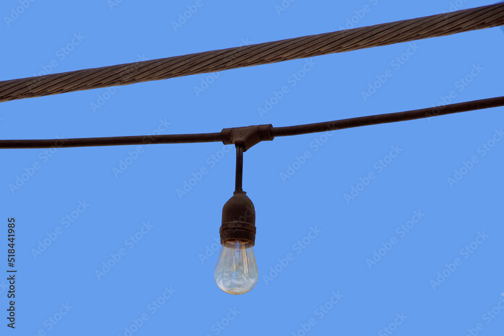 Obraz premium A single light bulb of an outdoor light chain seen against blue sky