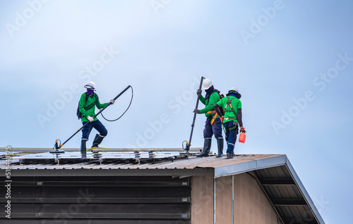 Group of professional cleaning service workers clean the solar panels on industrial building roof against cloudy sky background