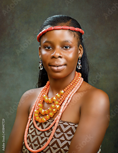 Portrait of a happy African girl, lady or model in a beautiful Nigerian traditional wear and beads necklace, posing for photograph in a studio with grey background photo