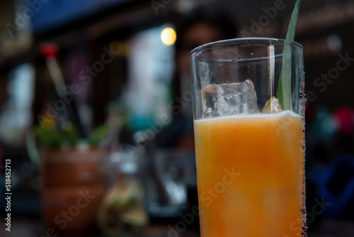 Yellow drink on a dark nightclub background. Close up of a glass of juice with ice and a leaf decoration. Yellow drink on a bar counter.