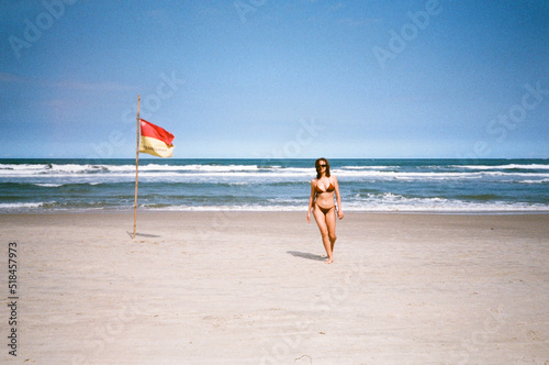 Woman in bikini walk in the sand at the beach next to a flag and water