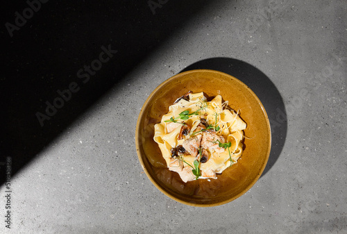 Italian pasta Pappardelle with chicken and mushrooms in creamy sauce on gray stone table. Creamy pasta pappardelle with chicken meat and mushroom. Fettucine fungi on concrete background with shadow. photo