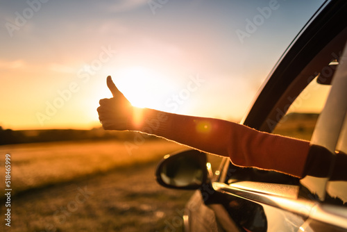 Getting away from it all. Happy person woman on a road trip with thumbs up arms out of the car facing a beautiful sunset.  photo