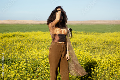 Young girl with curly hair posing in a flowers field holding accessory photo