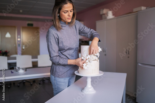 young pastry chef decorating a beautiful cake in her pastry shop photo