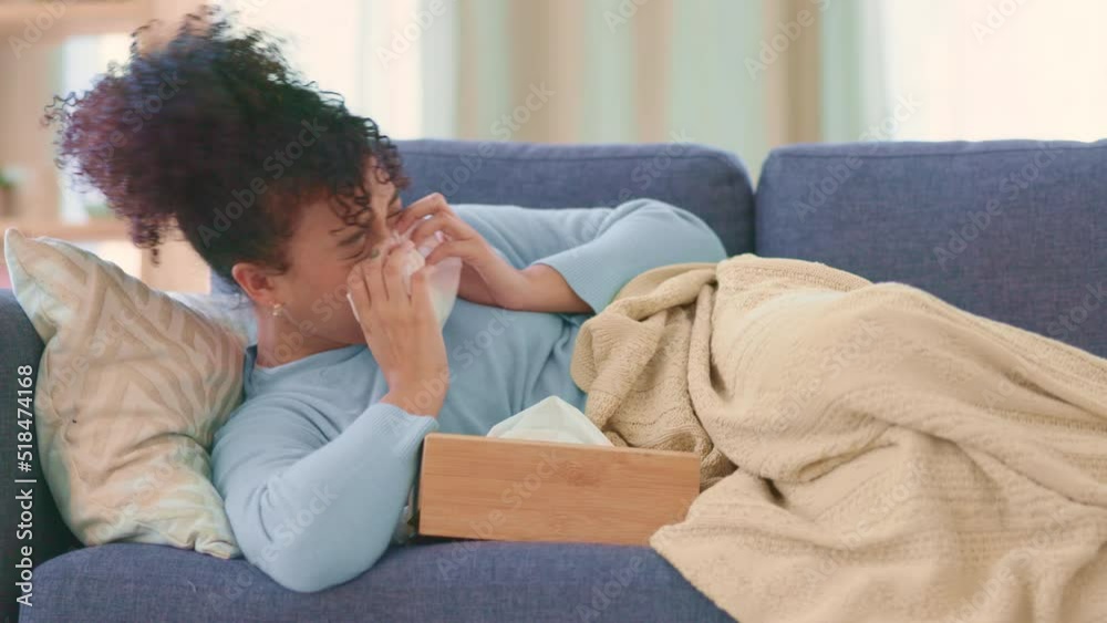 Woman sick with the flu on a couch at home, sneezing and blowing nose. Young female suffering from sinus, allergy or Covid19 while isolating. Lady taking off from work to recover from seasonal cold Woman sick with the flu on a couch at home, sneezing and blowing nose. Young female suffering from sinus, allergy or Covid19 while isolating. Lady taking off from work to recover from seasonal cold