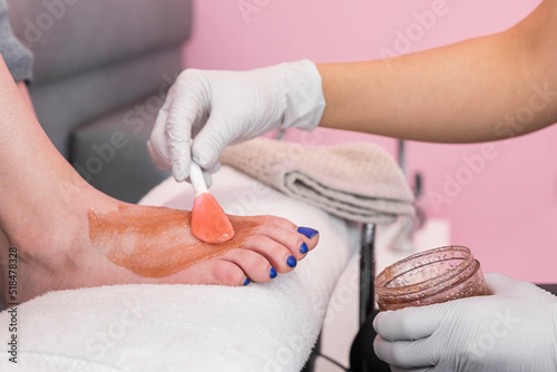 female hands with white gloves applying wax to a woman feet photo