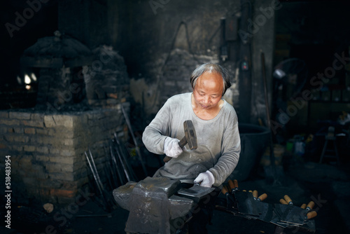 An East Asian Ironworker manufactures a Chinese kitchen knife.