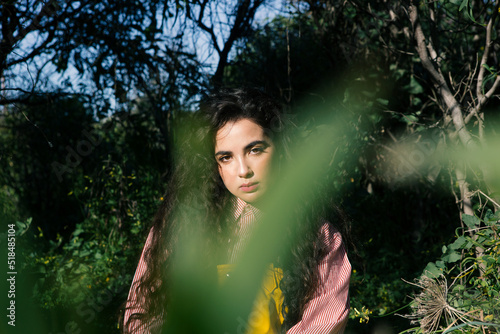 Beautiful young girl with long black hair sitting between the trees  photo