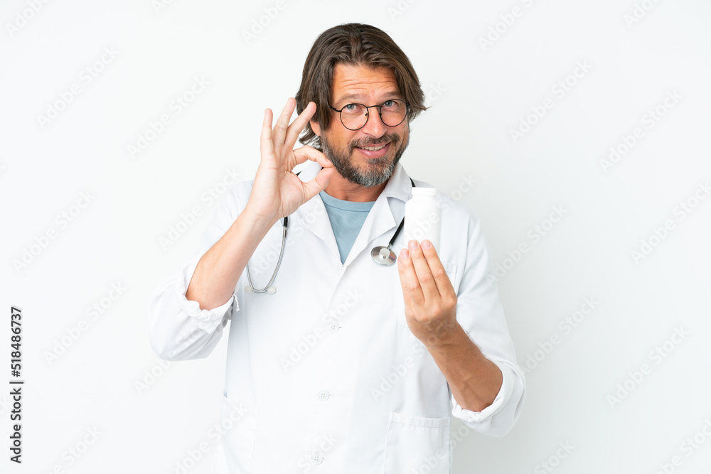 Senior dutch man isolated on white background wearing a doctor gown and holding pills Senior dutch man isolated on white background wearing a doctor gown and holding pills