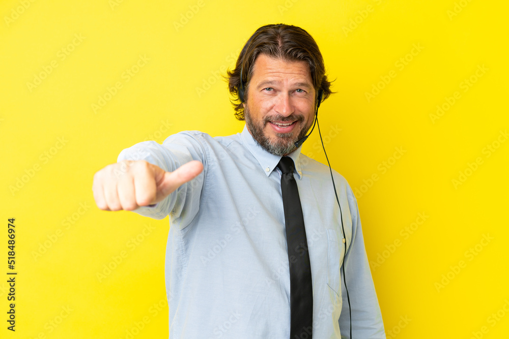 Telemarketer dutch man working with a headset isolated on yellow background giving a thumbs up gesture