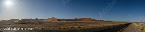 A panorama of dunes in the Namib Desert, on the way to Sossusvlei. Road in the foreground with blue sky.