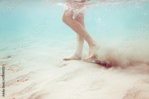 Underwater woman feet walking on tropical sea bottom photo