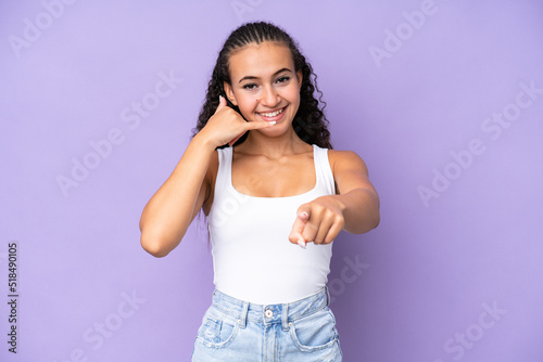 Young woman isolated on purple background making phone gesture and pointing front