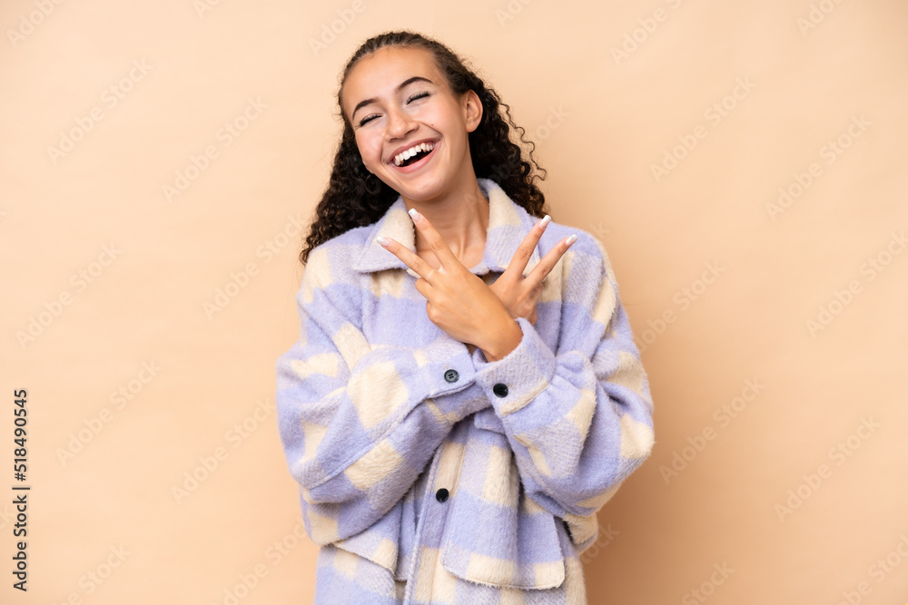 Young woman isolated on beige background smiling and showing victory sign Young woman isolated on beige background smiling and showing victory sign