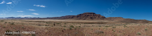 A panoramic photo of a hill/mountain in the middle of Namibia. Blue sky with scattered blue clouds.