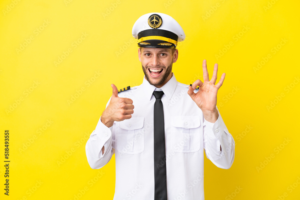 Airplane caucasian pilot isolated on yellow background showing ok sign and thumb up gesture
