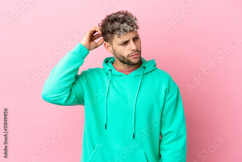 Young handsome caucasian man isolated on pink background having doubts while scratching head © luismolinero
