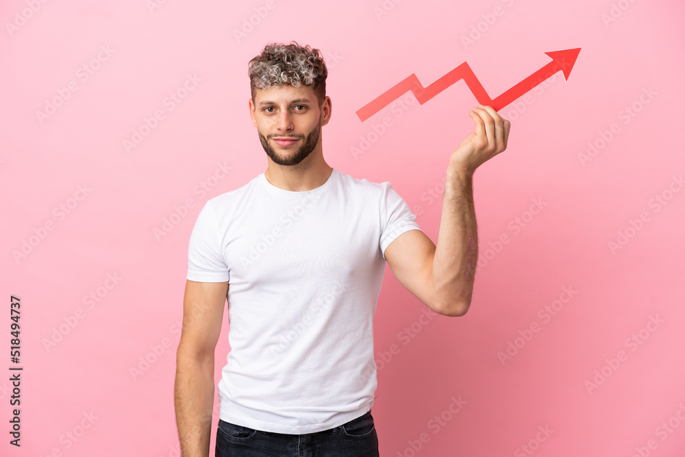 Young handsome caucasian man isolated on pink background holding a catching a rising arrow with happy expression Young handsome caucasian man isolated on pink background holding a catching a rising arrow with happy expression