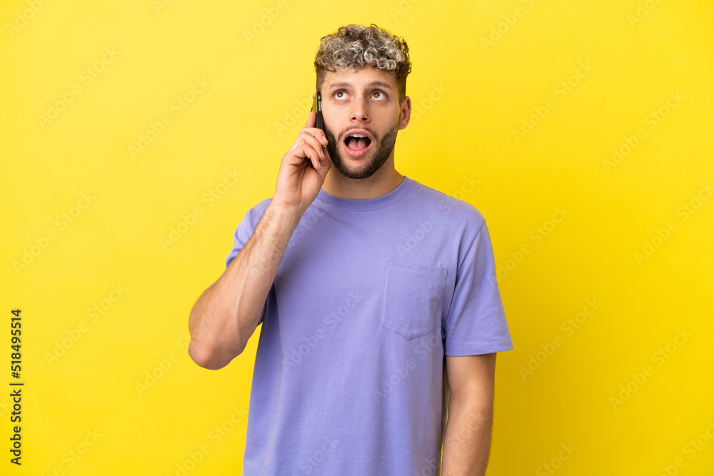 Young caucasian man using mobile phone isolated on yellow background looking up and with surprised expression Young caucasian man using mobile phone isolated on yellow background looking up and with surprised expression
