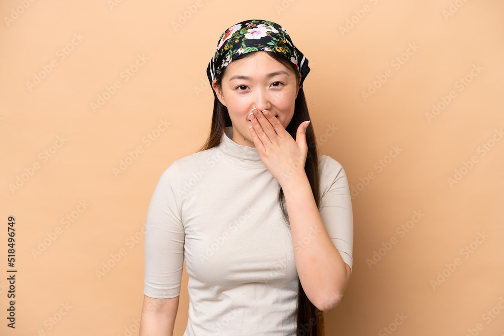 Young Chinese woman isolated on beige background happy and smiling covering mouth with hand