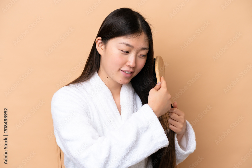 Young Chinese woman isolated on beige background with hair comb Young Chinese woman isolated on beige background with hair comb