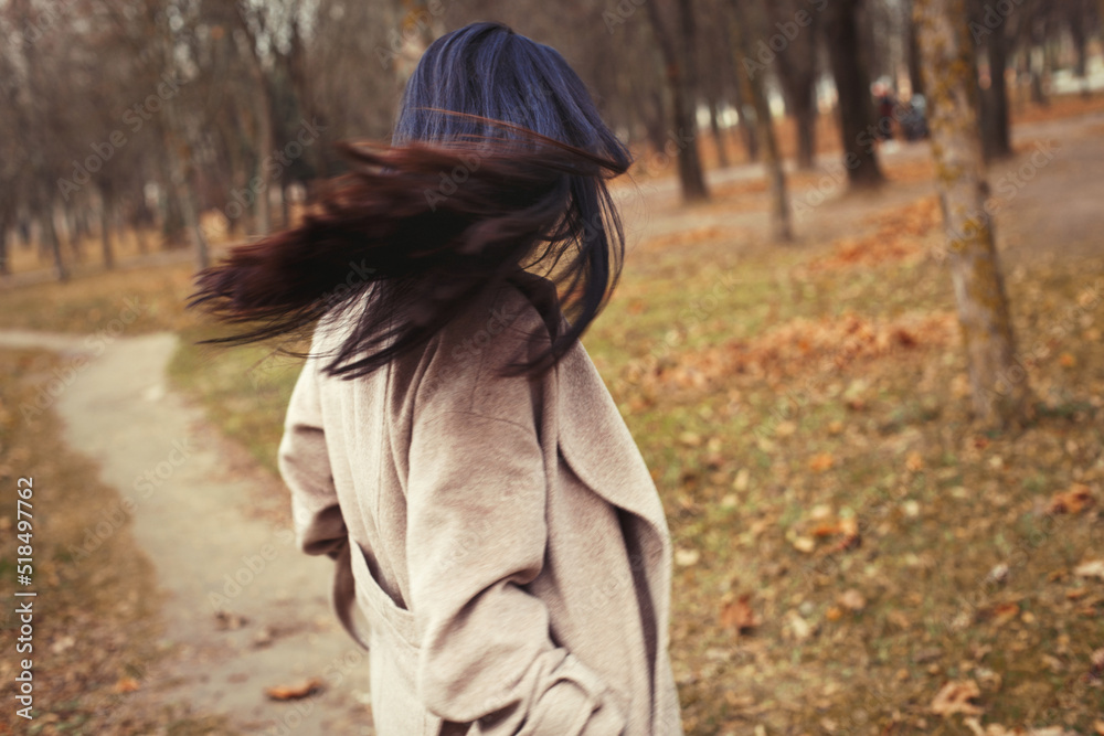 portrait of brunette hair woman in beige coat walking at the city park .