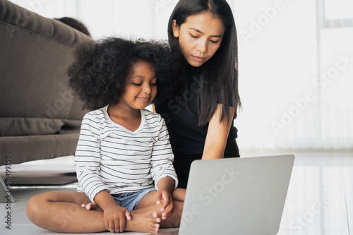 A little girl African Asian Playing on a laptop computer in the living room. Mom takes care closely So that her daughter can use technology correctly and appropriately for the age.