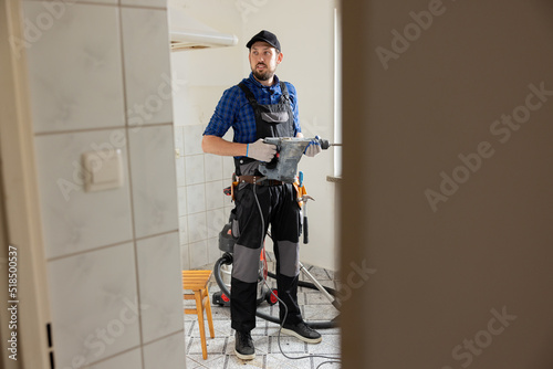 A man in a baseball cap wearing a work suit works in construction while renovating an apartment renovates a bathroom at home holds a hammer in hands.