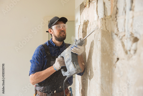 A focused man puts all strength while hammering tiles in kitchen bathroom. A man working on a house construction site during a renovation performs finishing work with protective goggles gloves.