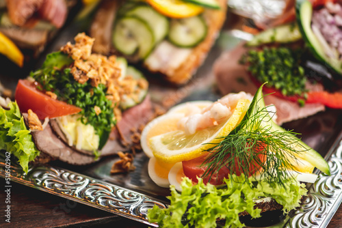 Danish traditional Smørrebrød or open sandwiches served in a plate, roast beef with remoulade, tomato and shredded horseradish on Danish rye bread, egg, prawns, lemon and mayonnaise photo