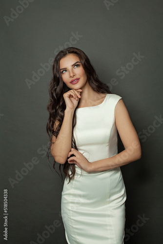 Cute glamorous woman fashion model wearing white silky dress looking up on black background © millaf