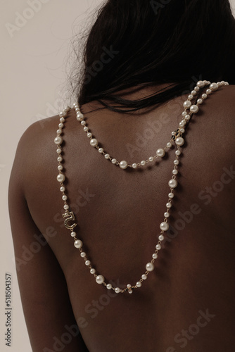 Close-up of beautiful woman back with pearl necklace on tan skin indoor. Mock-up