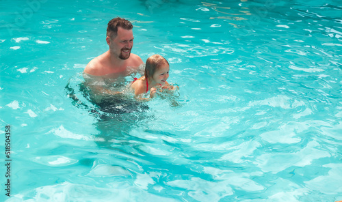 Happy family father with daughter together, swimming in swim pool during summer vacation
