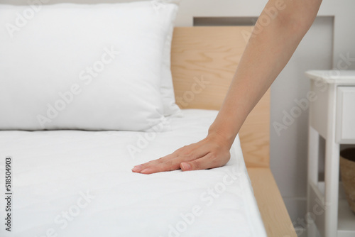 Woman touching soft white mattress on bed indoors, closeup
