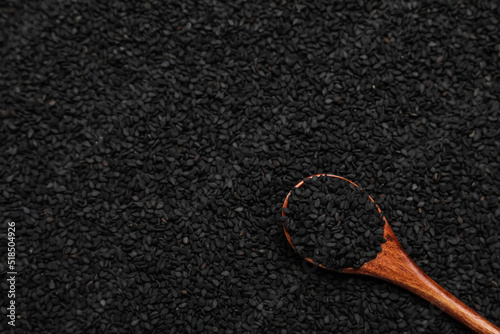 Wooden spoon on pile of black sesame seeds, top view. Space for text