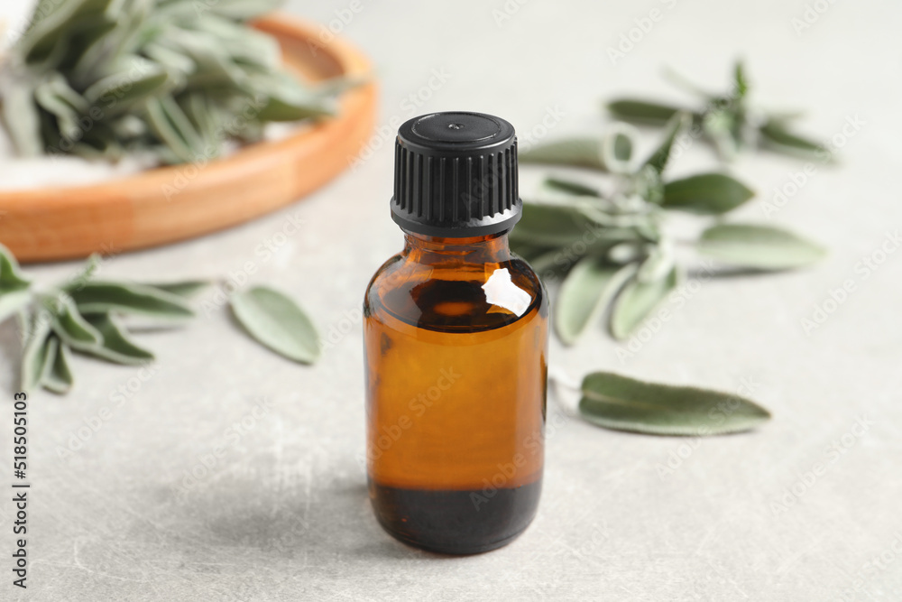 Bottle of essential sage oil and leaves on light grey table Bottle of essential sage oil and leaves on light grey table
