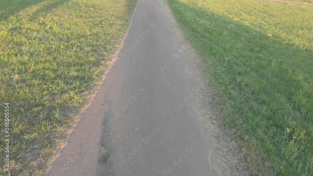 Drone landing on asphalt road between two green fields with drone shadow visible in the end of landing, drone lands on rural road on sunset Drone landing on asphalt road between two green fields with drone shadow visible in the end of landing, drone lands on rural road on sunset