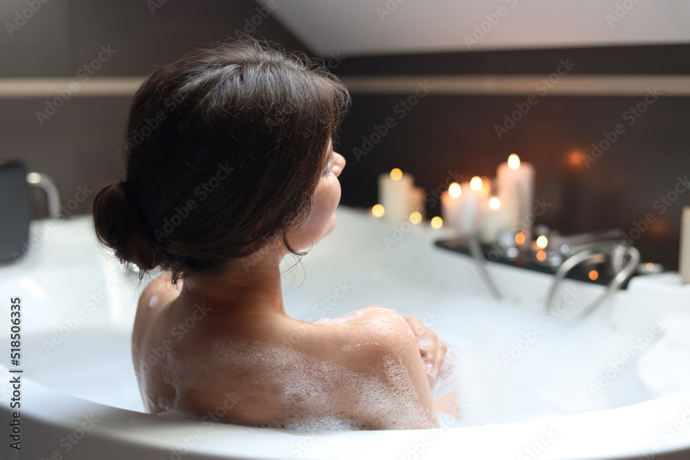 Young woman taking bubble bath, back view. Romantic atmosphere Young woman taking bubble bath, back view. Romantic atmosphere