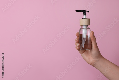 Woman holding bottle of cosmetic product on pink background, closeup. Space for text