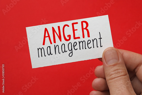 Man holding card with words Anger Management on red background, closeup