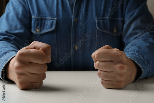 Foto Man clenching fists at table while restraining anger, closeup