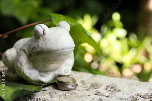 Frog figure with coins on stone parapet outdoors. Space for text