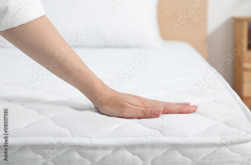 Obraz na płótnie Woman touching soft white mattress on bed indoors, closeup