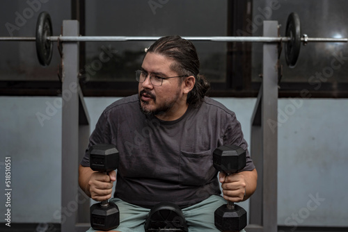 A man in his late 30s at the gym resting in between sets. Contemplating about his next exercise. A dad getting back in shape.