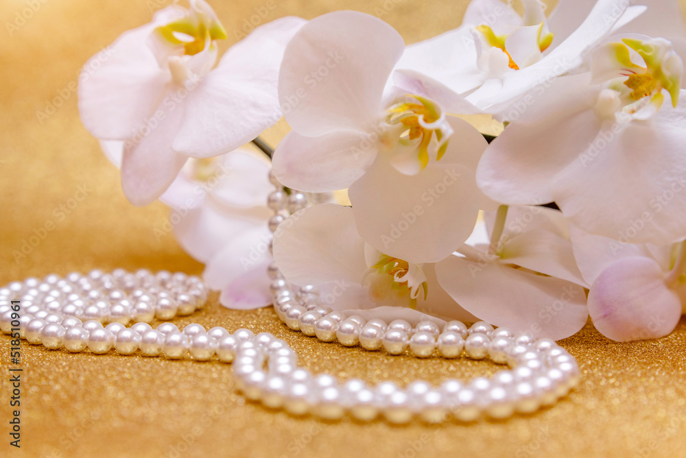 white Orchid and pearl necklace on a shiny gold background white Orchid and pearl necklace on a shiny gold background