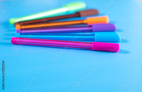Selective focus shot of many colorful pens lying on blue colored background. 
