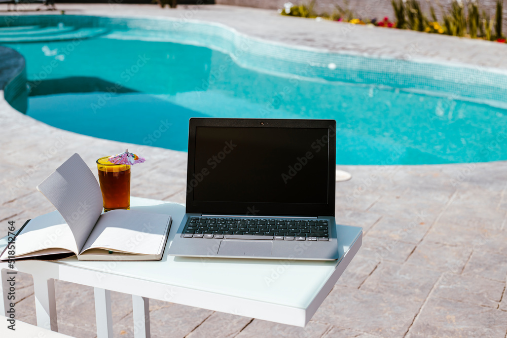 laptop, notepad and cool drink by the pool, working from home