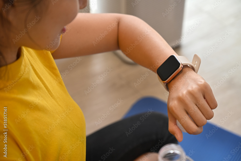 Obraz premium Sporty woman checking fitness results or heart rate on her smartwatch during exercising at home