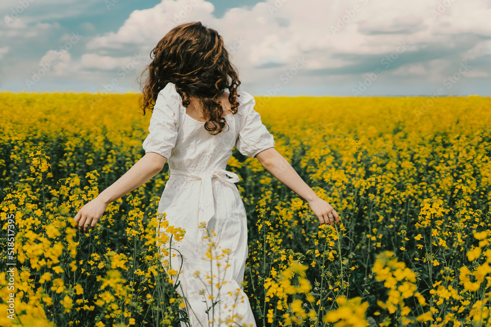 A girl in a white dress and curly hair runs across a field of yellow flowers. A girl in a white dress and curly hair runs across a field of yellow flowers.